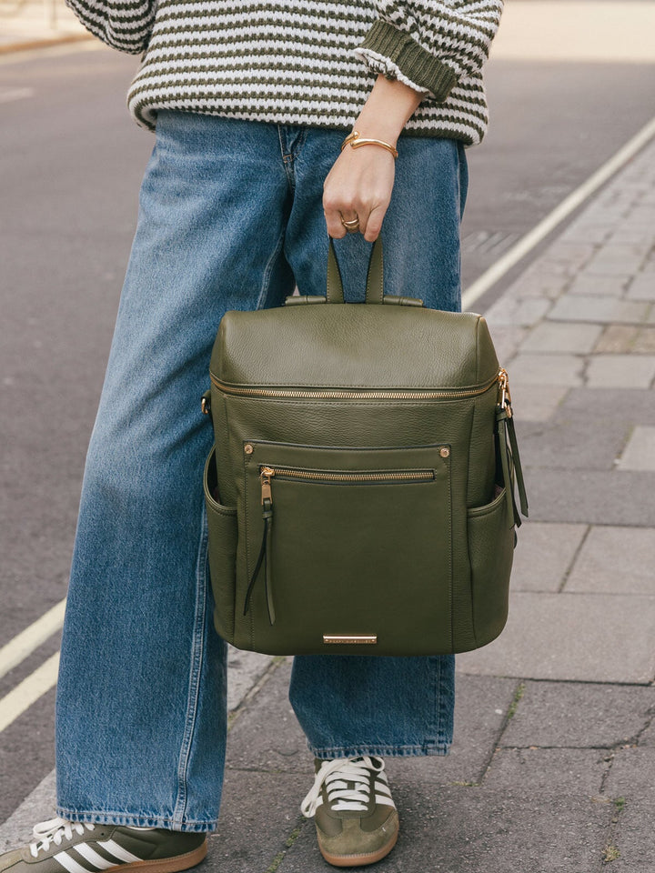 Woman holding the Poppy & Peonies Commuter Backpack in Olive by the top handle while standing on a city street.