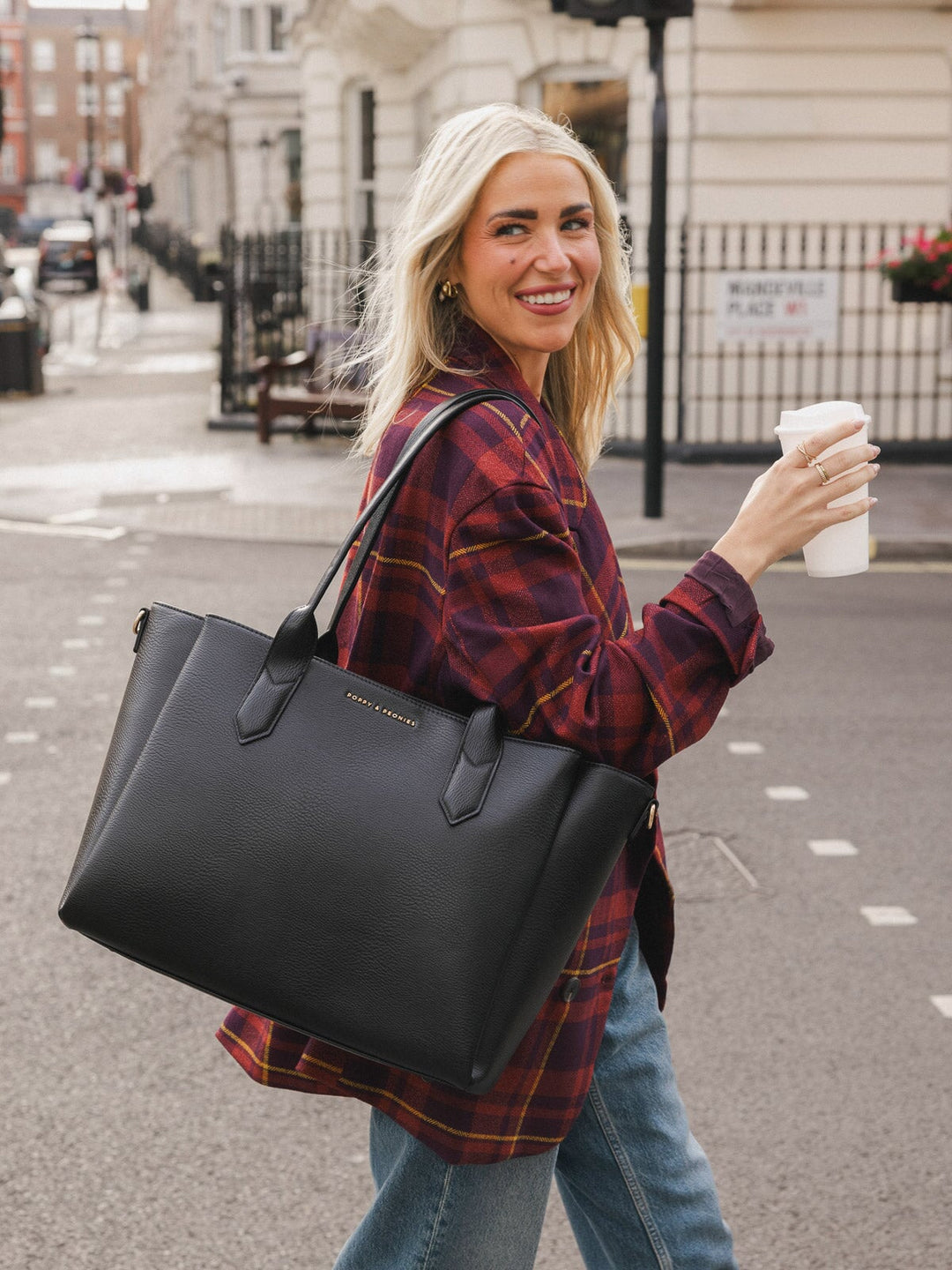 Close-up of woman carrying the Poppy & Peonies Double Duty Tote in Black over her shoulder while holding a takeaway coffee.