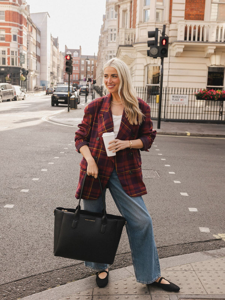 Woman carrying the Poppy & Peonies Double Duty Tote in Black by the top handles while holding a takeaway coffee on a city street.