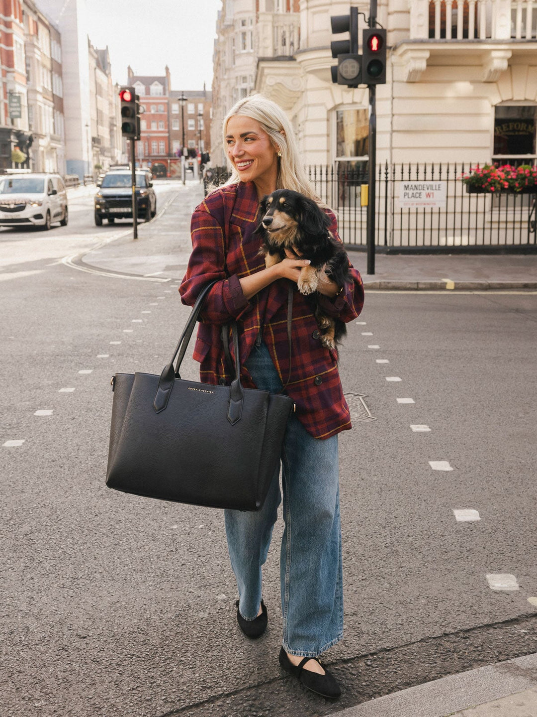 Woman walking with the Poppy & Peonies Double Duty Tote in Black carried by the top handles while holding a small dog.