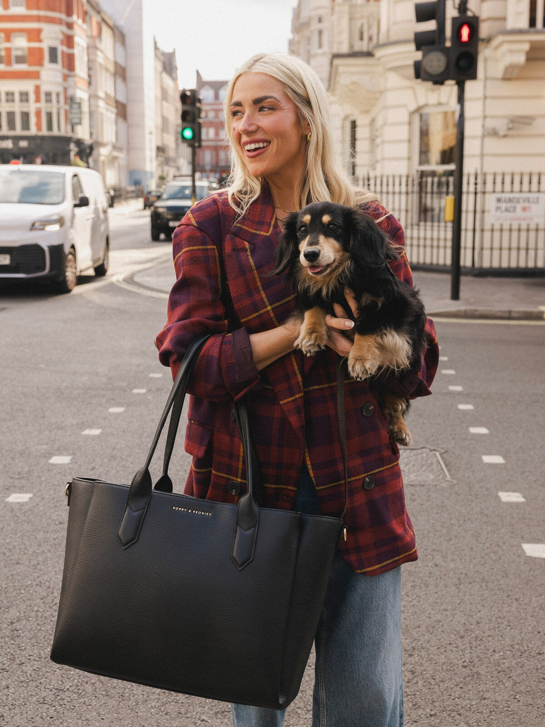 Close-up of a woman carrying the Poppy & Peonies Double Duty Tote in Black by the top handles while holding a small dog.