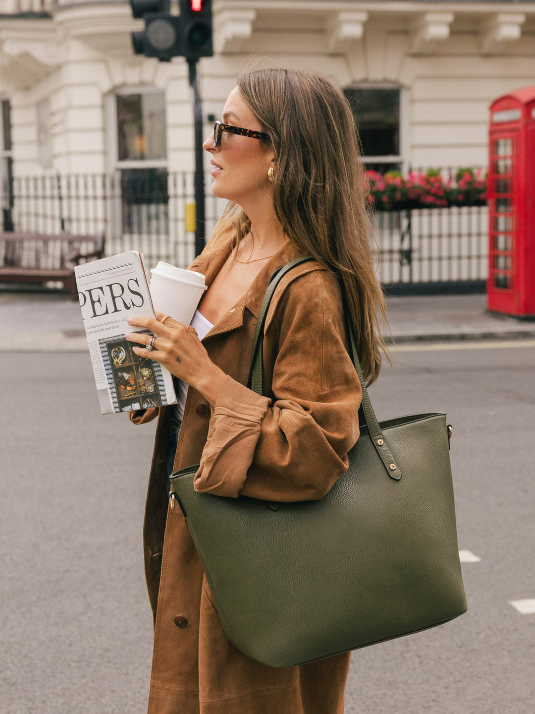 Woman carrying the Poppy & Peonies Go-Getter Tote in Olive over her shoulder while holding a takeaway coffee and magazine outdoors.