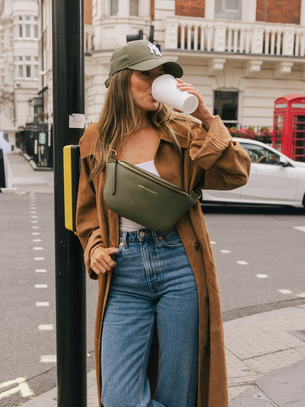 Woman wearing the Poppy & Peonies Sidekick in Olive crossbody while drinking a takeaway coffee outdoors.