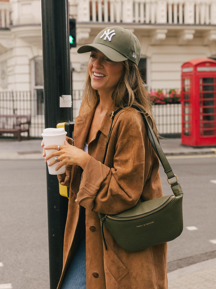 Woman carrying the Poppy & Peonies Sidekick in Olive over her shoulder while holding a takeaway coffee on a city street.