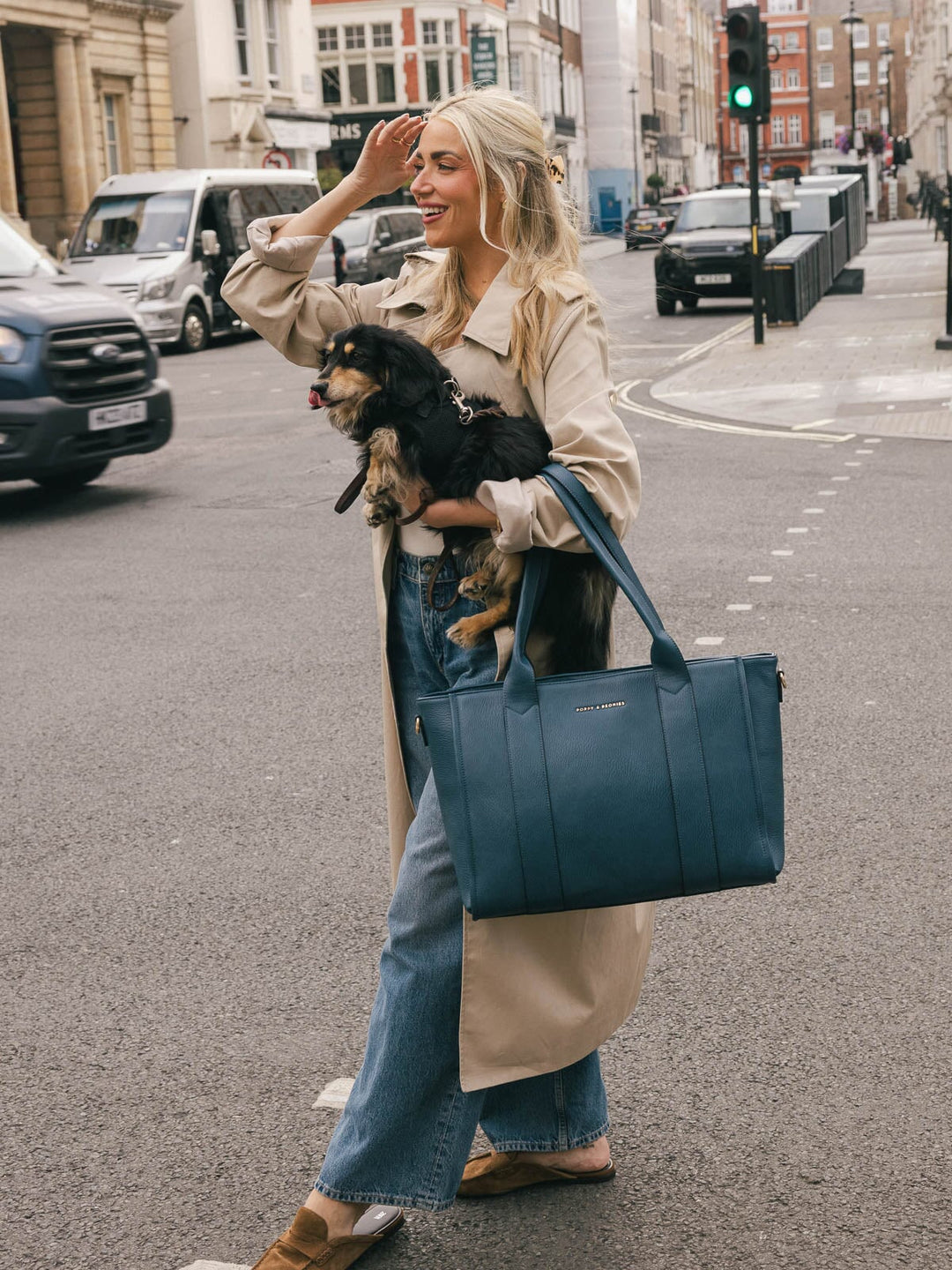 Woman carrying the Poppy & Peonies Multitasker in Navy by the top handles while holding a small dog on a city street.