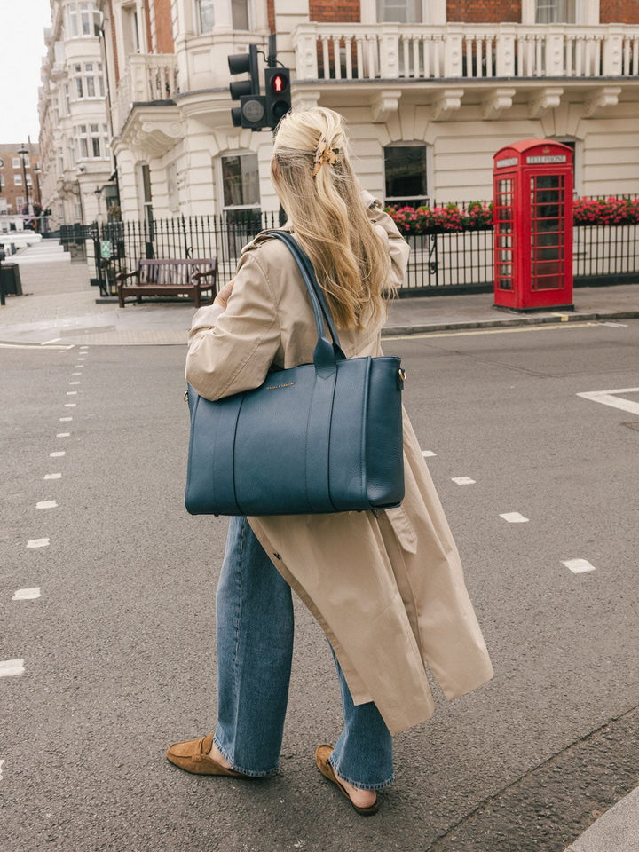 Woman carrying the Poppy & Peonies Multitasker in Navy over her shoulder while walking on a city street.