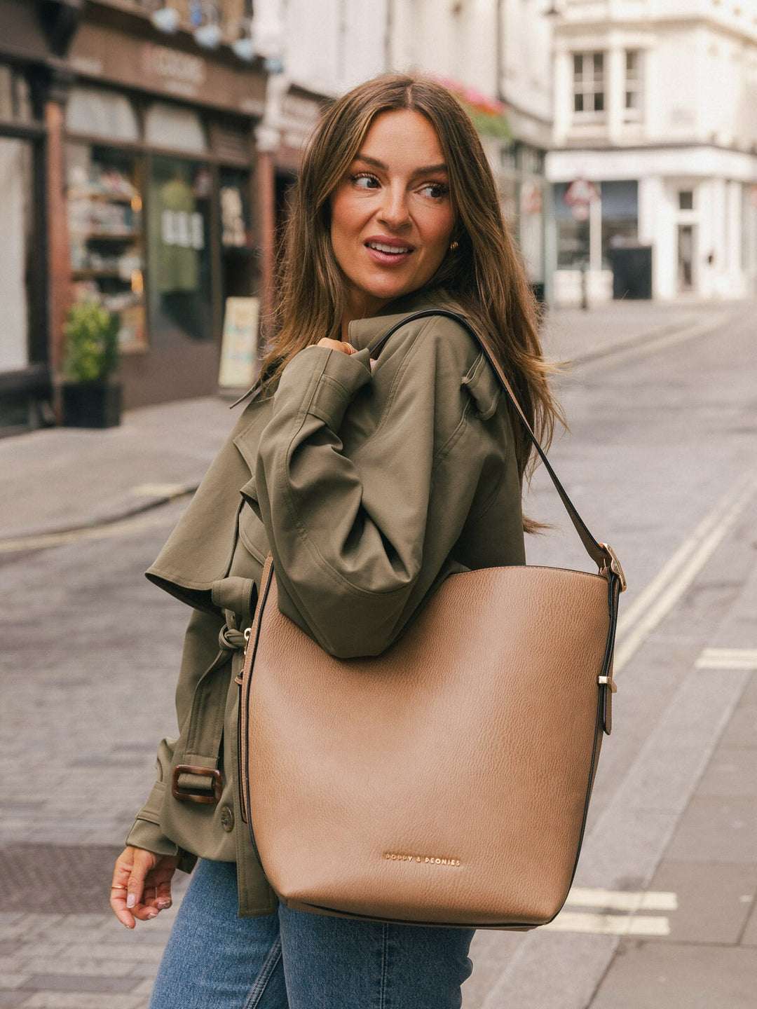 Close-up lifestyle shot of a woman carrying the Poppy & Peonies Bucket Bag in Taupe over her shoulder on a city street.
