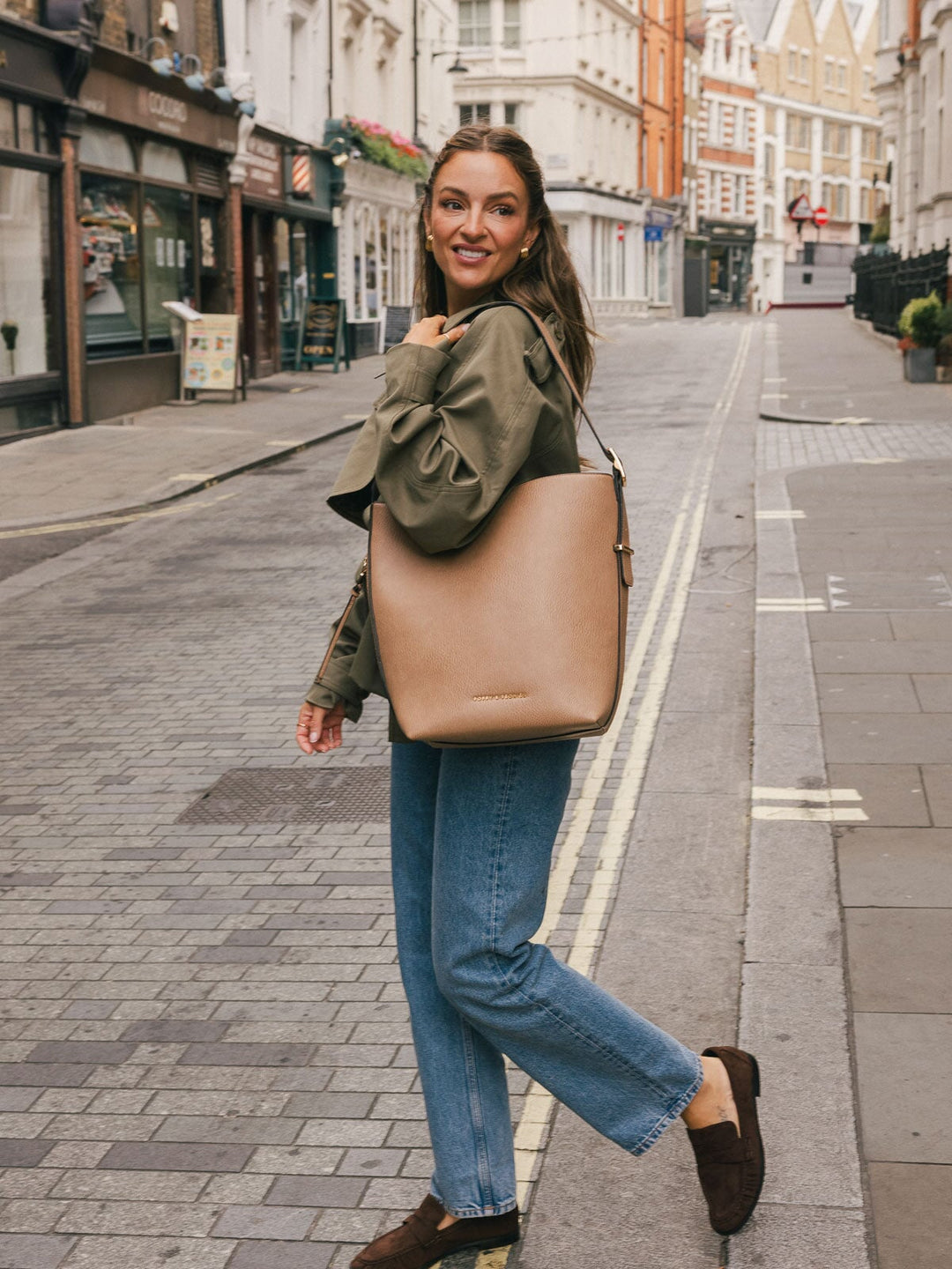 Full-body street-style shot of a woman carrying the Poppy & Peonies Bucket Bag in Taupe over her shoulder.