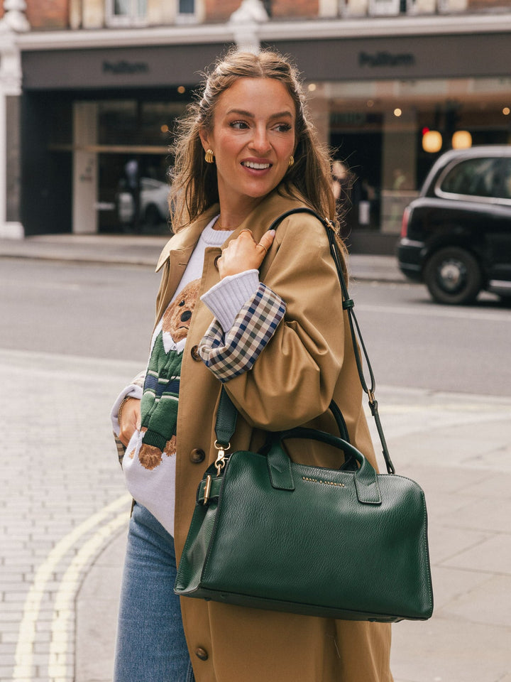 Mid-length street-style shot of a woman carrying the Poppy & Peonies Mini Uptown Tote in Heritage Green over her arm.