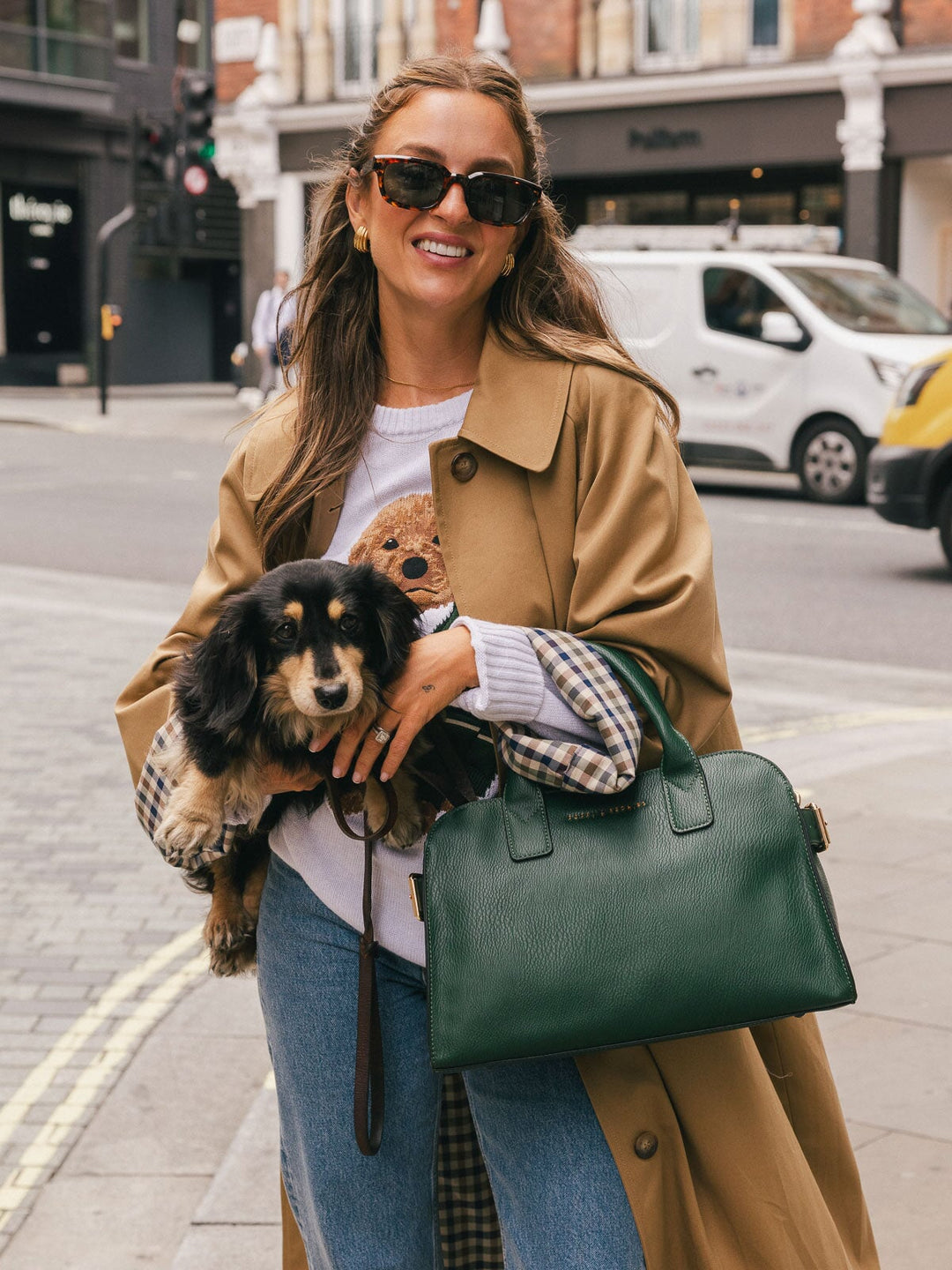 Mid-length lifestyle shot of a woman carrying the Poppy & Peonies Mini Uptown Tote in Heritage Green by the top handles while holding a small dog.