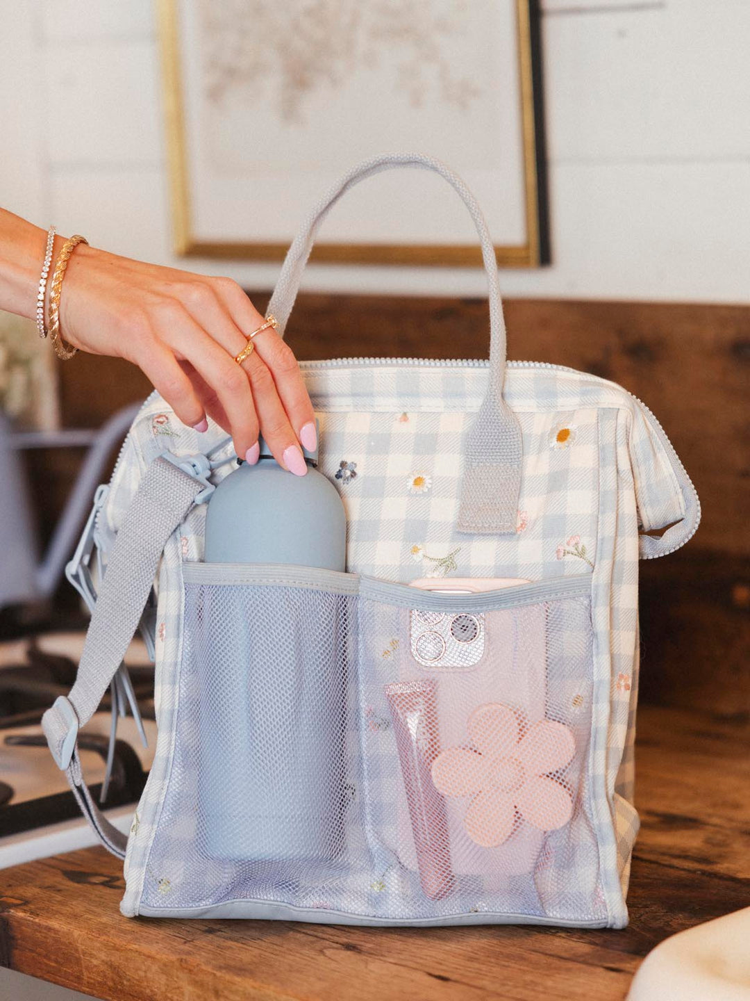 Hand removing a water bottle from a gingham lunch bag