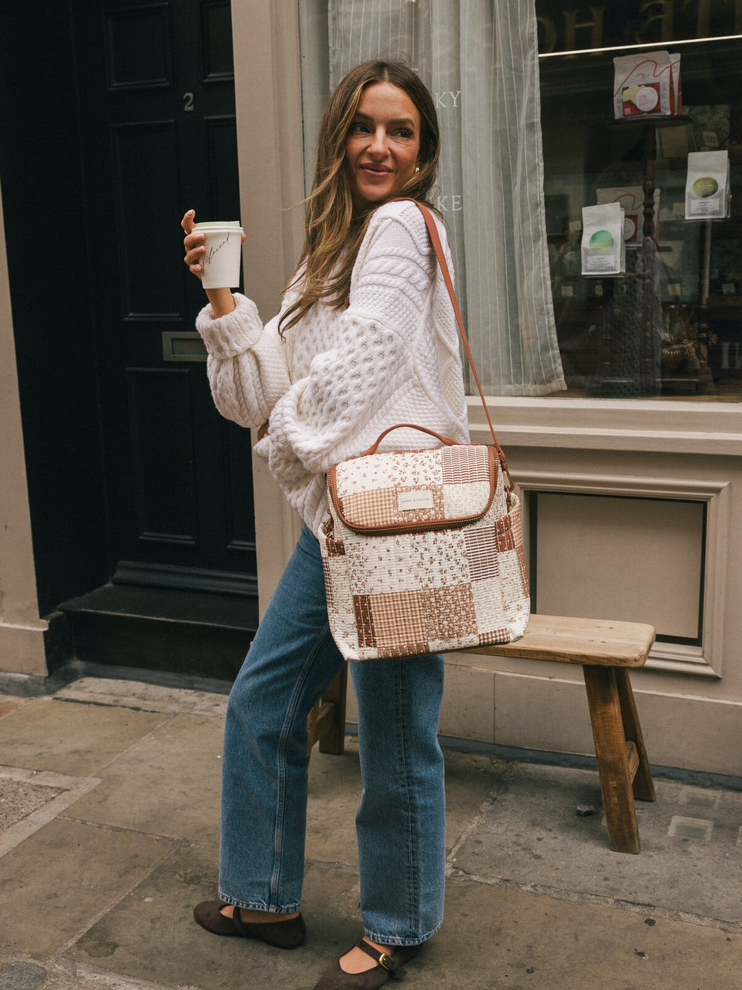 Full-body lifestyle shot of a woman wearing the Poppy & Peonies Lunch Date in Brown Patchwork over her shoulder while holding a takeaway coffee.