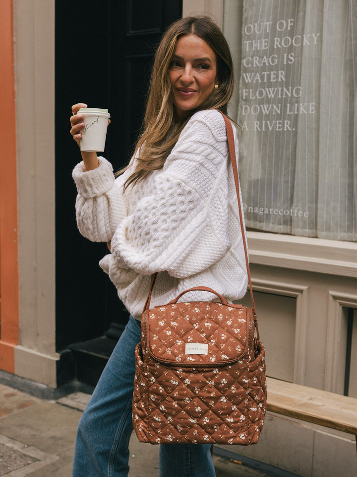 Lifestyle shot of a woman wearing the Poppy & Peonies Lunch Date in Brown Floral over her shoulder while holding a takeaway coffee.