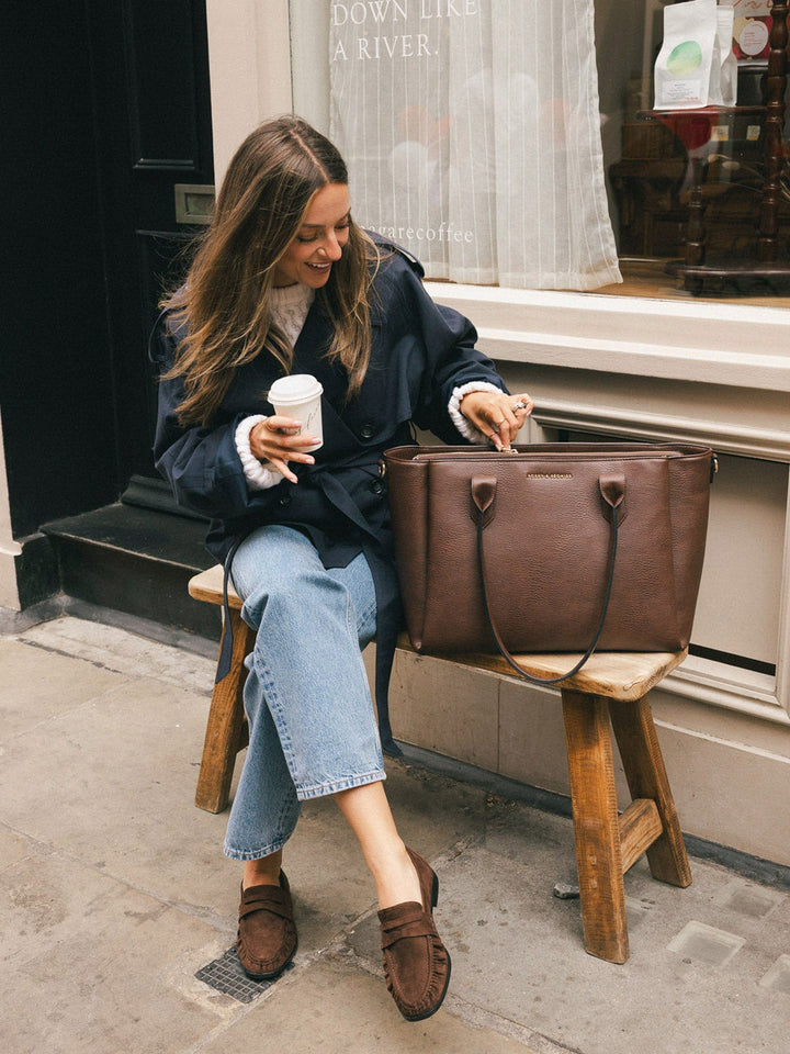 Woman sitting beside the Poppy & Peonies Double Duty Tote in Espresso opening the bag.
