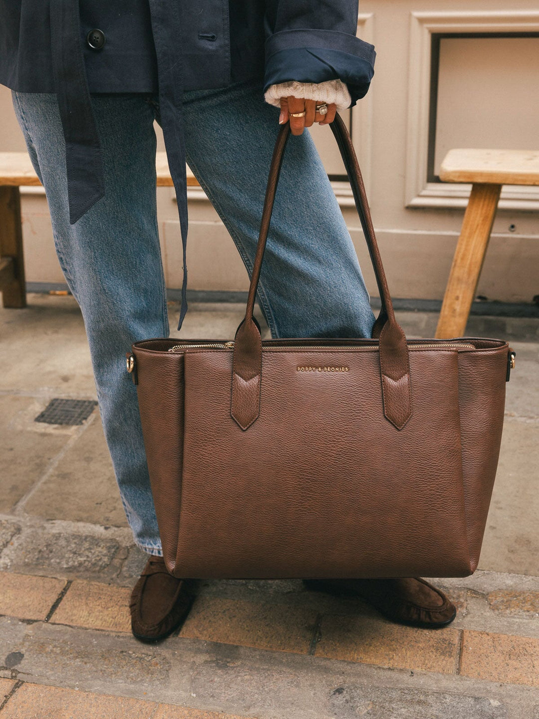 Close-up of a woman carrying the Poppy & Peonies Double Duty Tote in Espresso by the top handles over her shoulder.