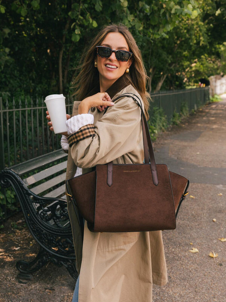 Close-up of Poppy & Peonies Mini Avenue Tote in Espresso Suede carried outdoors, showcasing its faux suede body, smooth vegan leather straps and compact shape.
