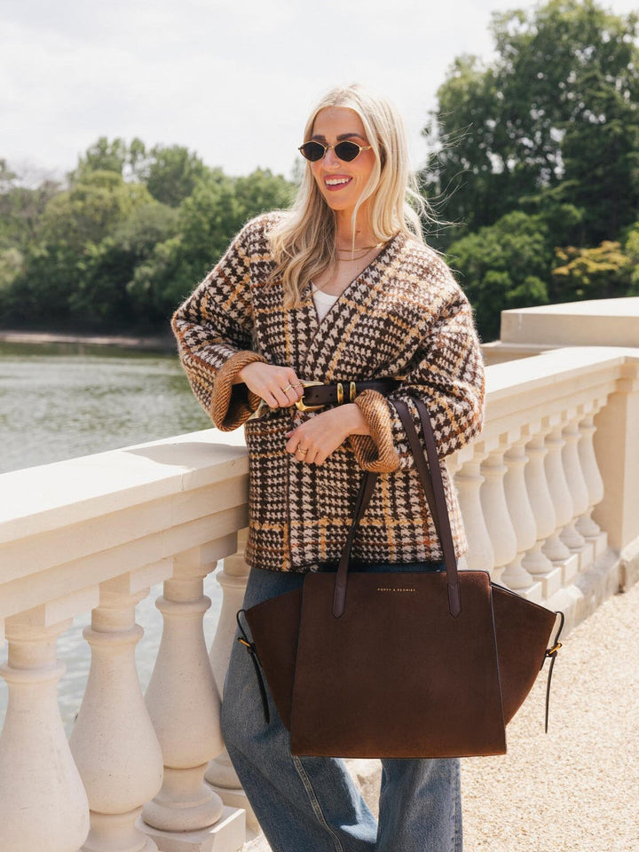 Poppy & Peonies Avenue Tote in Espresso Suede carried by hand beside a waterfront, showcasing its roomy silhouette and smooth vegan leather straps.