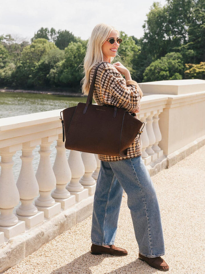 Poppy & Peonies Avenue Tote in Espresso Suede worn over the shoulder during a waterfront walk, showcasing its generous strap drop and spacious silhouette.