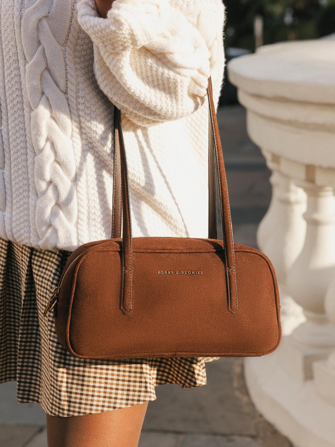 Close-up of Poppy & Peonies The Friday Satchel in Espresso Suede carried by the top handles, showcasing its elongated shape and rich brown suede texture.