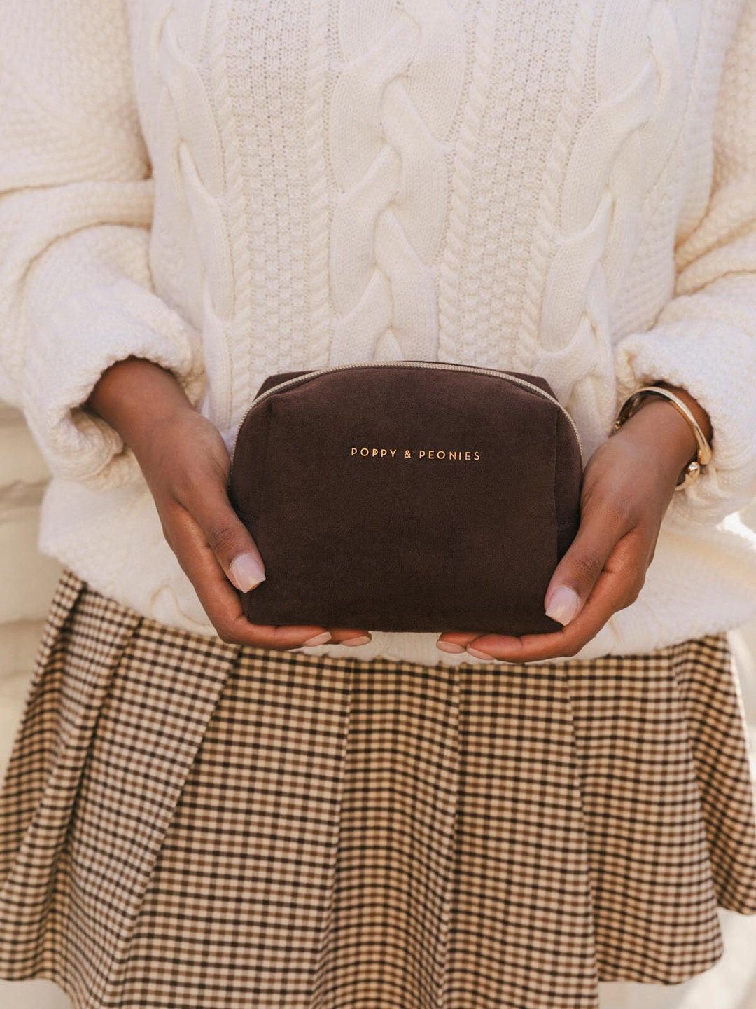 Poppy & Peonies Cosmetic Case in Espresso Suede held with both hands, showing its compact size, rounded shape and gold-tone logo.