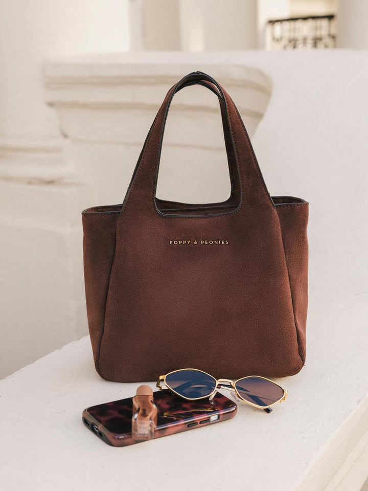 Poppy & Peonies The Pick Me Up Tote in Espresso Suede displayed on a ledge, featuring a soft structured silhouette, top handles and rich brown suede finish.