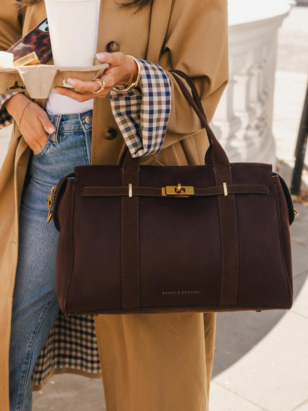 Close-up of Poppy & Peonies Effortless Tote in Espresso Suede carried by the top handles, showcasing its decorative turn-lock hardware, belting detail and rich suede exterior.