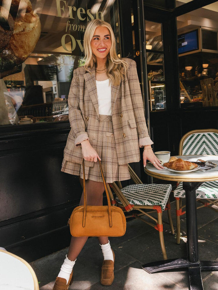 Poppy & Peonies The Friday Satchel in Cognac Suede carried by the top handles while standing outdoors, showcasing its structured silhouette.