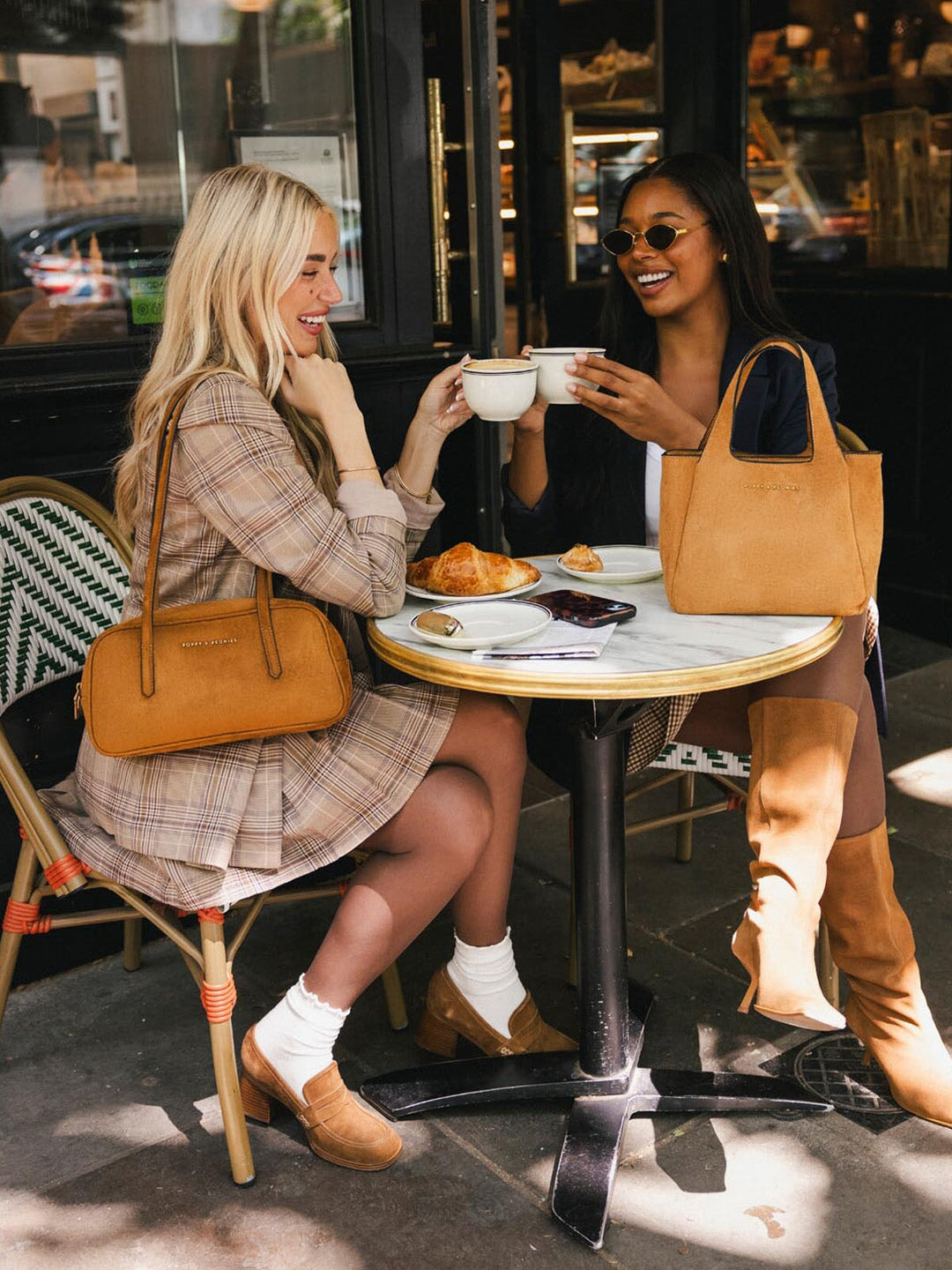 Poppy & Peonies The Pick Me Up Tote in Cognac Suede styled at an outdoor café, showcasing its warm suede finish and compact silhouette.
