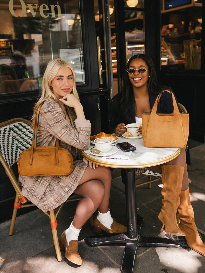 Poppy & Peonies The Pick Me Up Tote in Cognac Suede styled on an outdoor café table alongside with The Friday Satchel in Cognac Suede. 