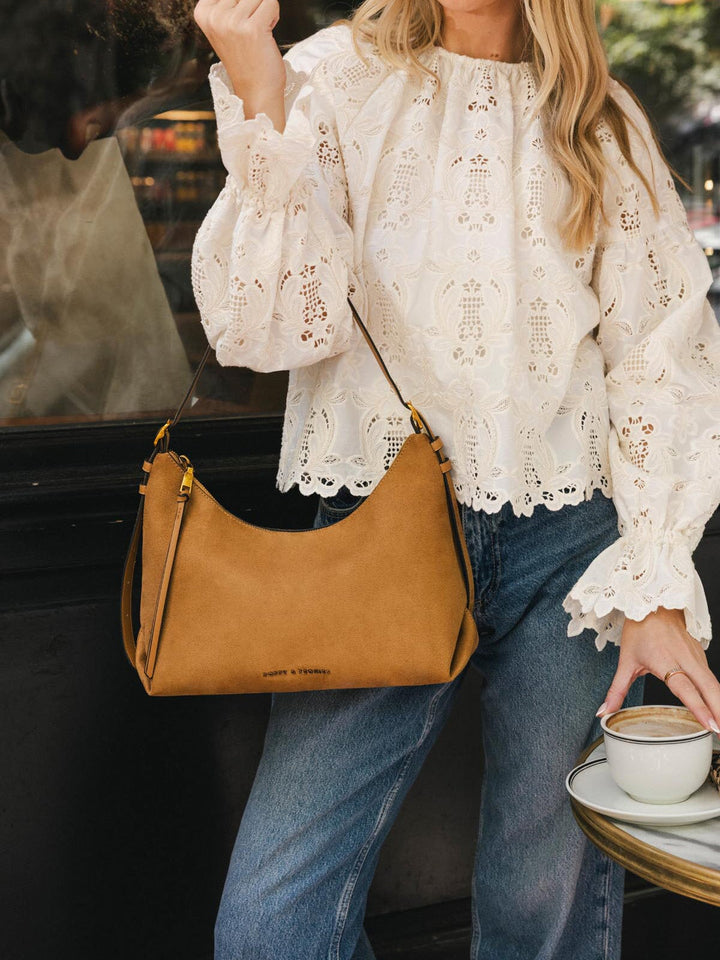 Close-up of Poppy & Peonies The Sunday Bag in Cognac Suede carried at the side, highlighting its soft suede exterior and gold-tone hardware.