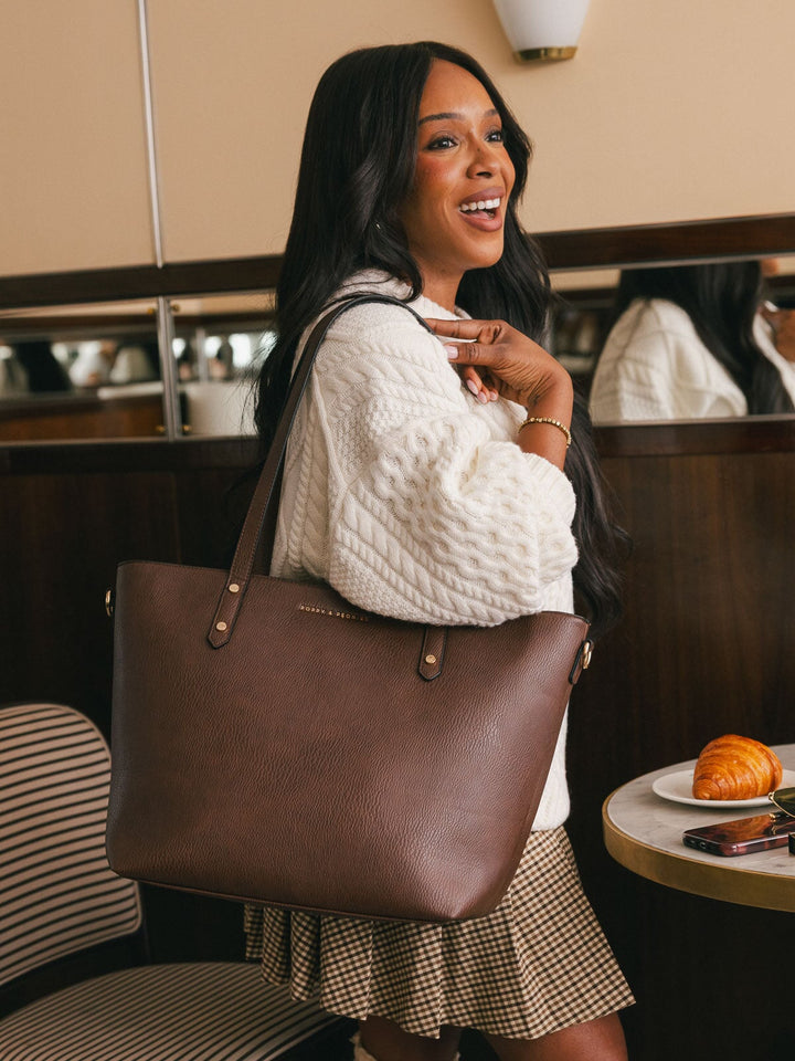 Lifestyle shot of a woman carrying the Poppy & Peonies Go-Getter Tote in Espresso over her shoulder inside a café.