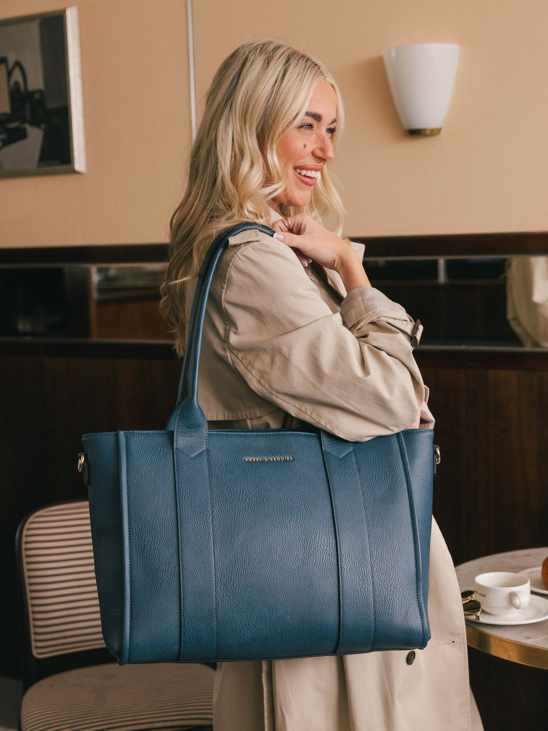 Lifestyle shot of a woman carrying the Poppy & Peonies Multitasker in Navy over her shoulder inside a café.