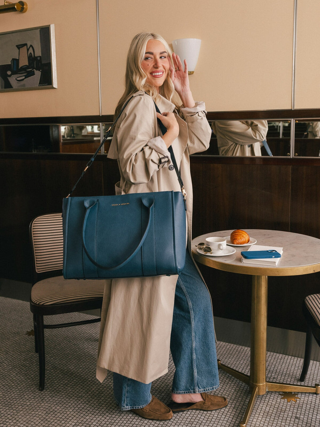 Lifestyle shot of a woman carrying the Poppy & Peonies Multitasker in Navy over her shoulder inside a café.