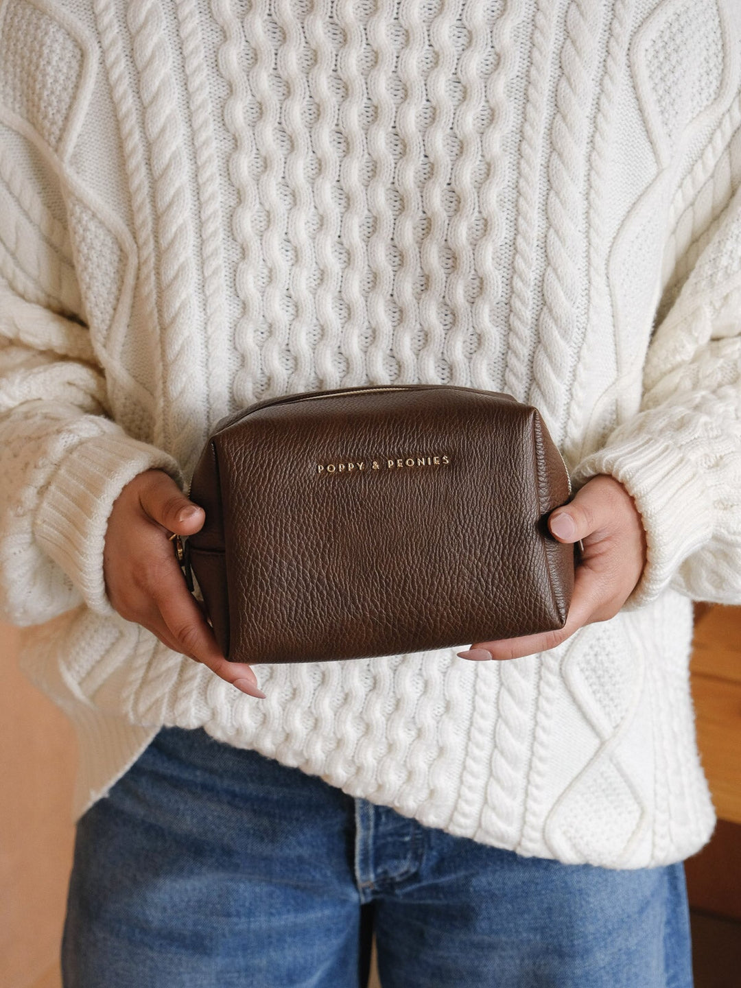 Product-focused lifestyle shot of a woman holding the Poppy & Peonies Cosmetic Case in Espresso, highlighting its rich brown finish and structured silhouette.