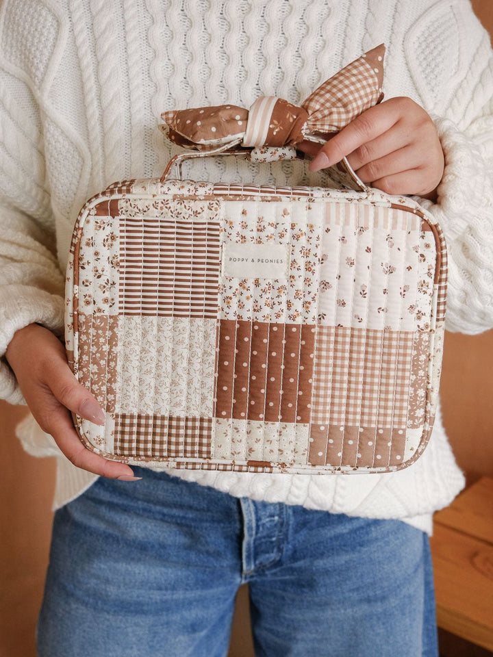 Front view of the Poppy & Peonies Hook Me Up Cosmetic Case in Brown Patchwork, featuring its brown and cream patchwork print, structured silhouette, and bow-detailed handle.