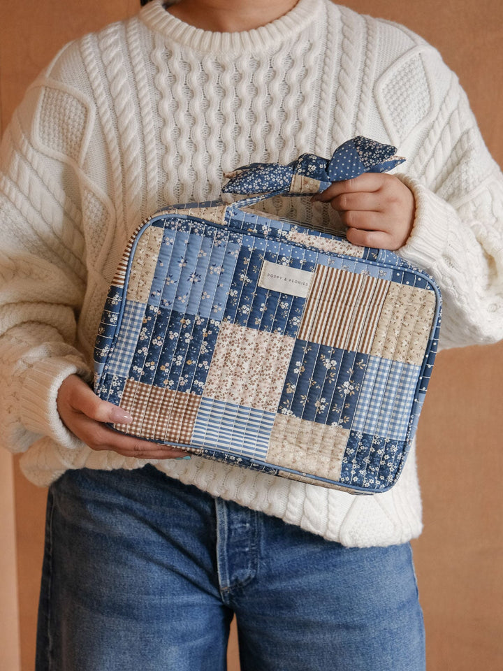 Lifestyle close-up of the Hook Me Up Cosmetic Case in Navy Patchwork, highlighting its mix of blue and neutral patchwork prints, zip-around closure, and signature bow handle.