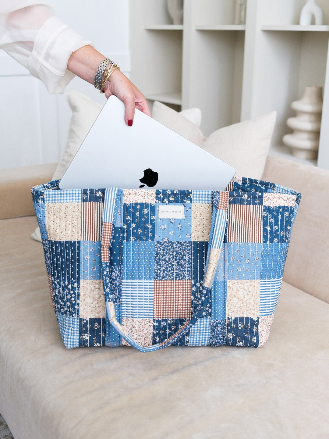 Lifestyle shot of the Daydreamer Tote in Navy Patchwork with a laptop being placed inside, highlighting its spacious design and structured top handles.