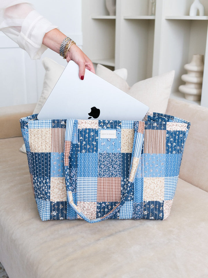 Lifestyle shot of the Daydreamer Tote in Navy Patchwork with a laptop being placed inside, highlighting its spacious design and structured top handles.