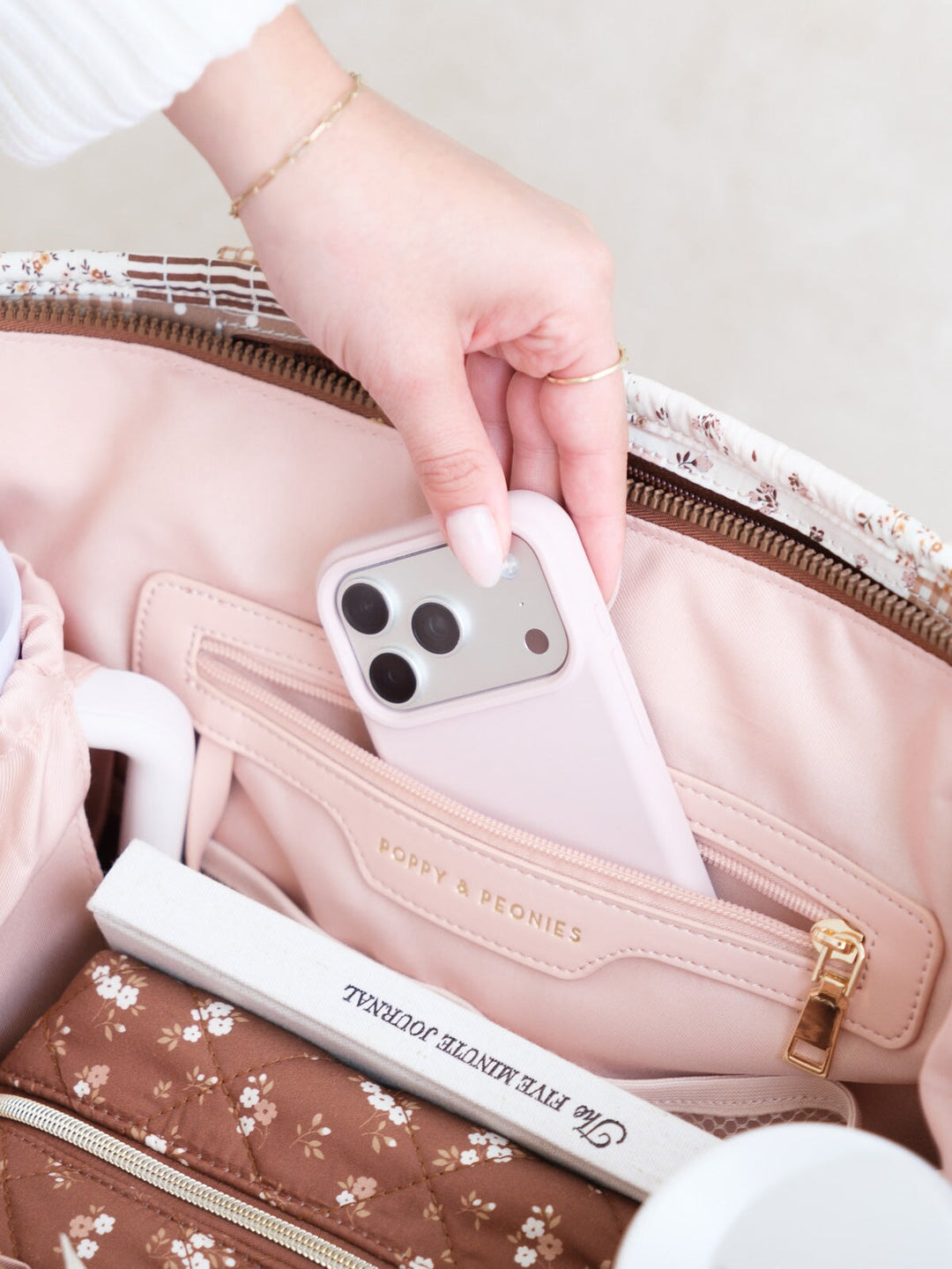 Close-up of the Daydreamer Tote in Brown Patchwork showing a phone being placed into an interior zip pocket alongside neatly organized daily essentials.