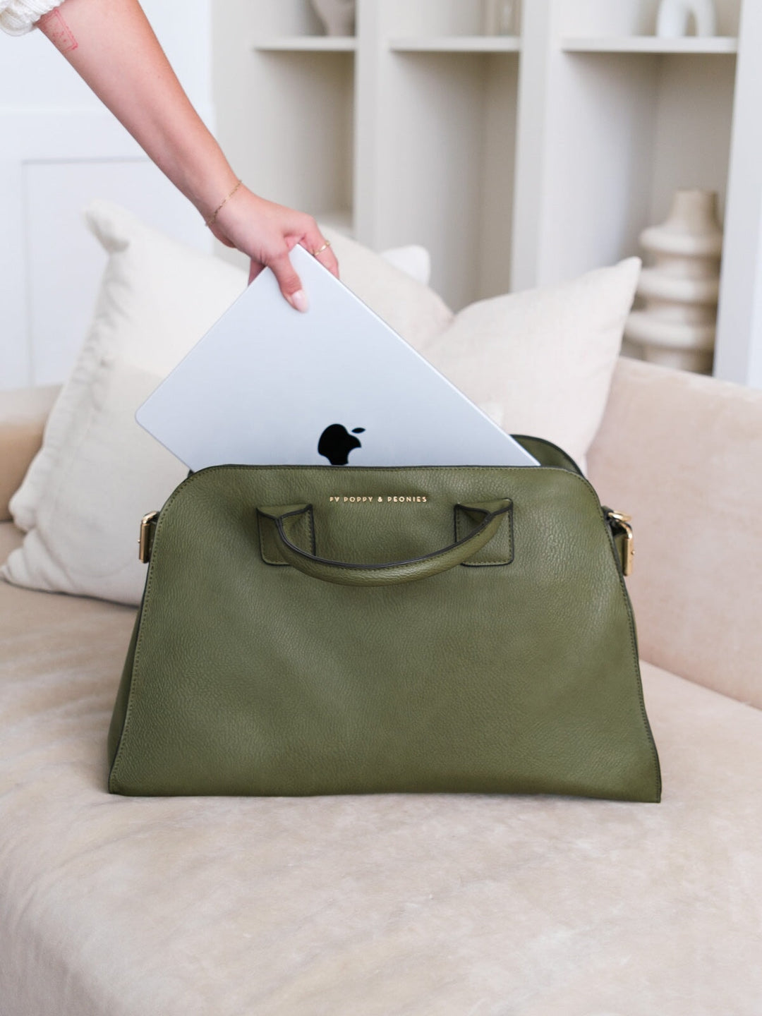 Lifestyle shot of the Uptown Tote in Olive with a laptop being placed inside, showcasing its structured silhouette and spacious design.