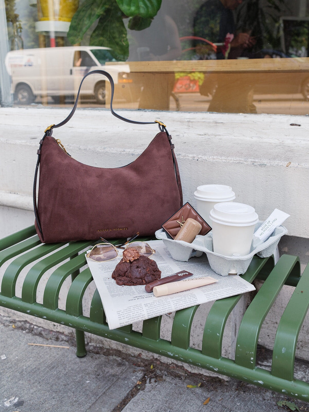 Poppy & Peonies The Sunday Bag in Espresso Suede displayed on an outdoor bench beside coffee and pastries, showcasing its relaxed silhouette and rich brown suede exterior.