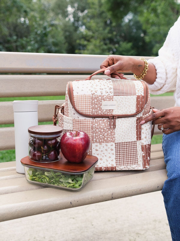 Poppy & Peonies The Lunch Date in Brown Patchwork opened beside packed lunch containers and snacks on a park bench.