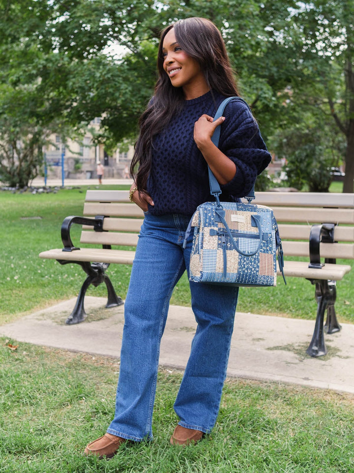 Lifestyle shot of a woman carrying the Poppy & Peonies The Lunch Bag in Navy Patchwork by its top handles, showing the bag’s size and proportions when carried.