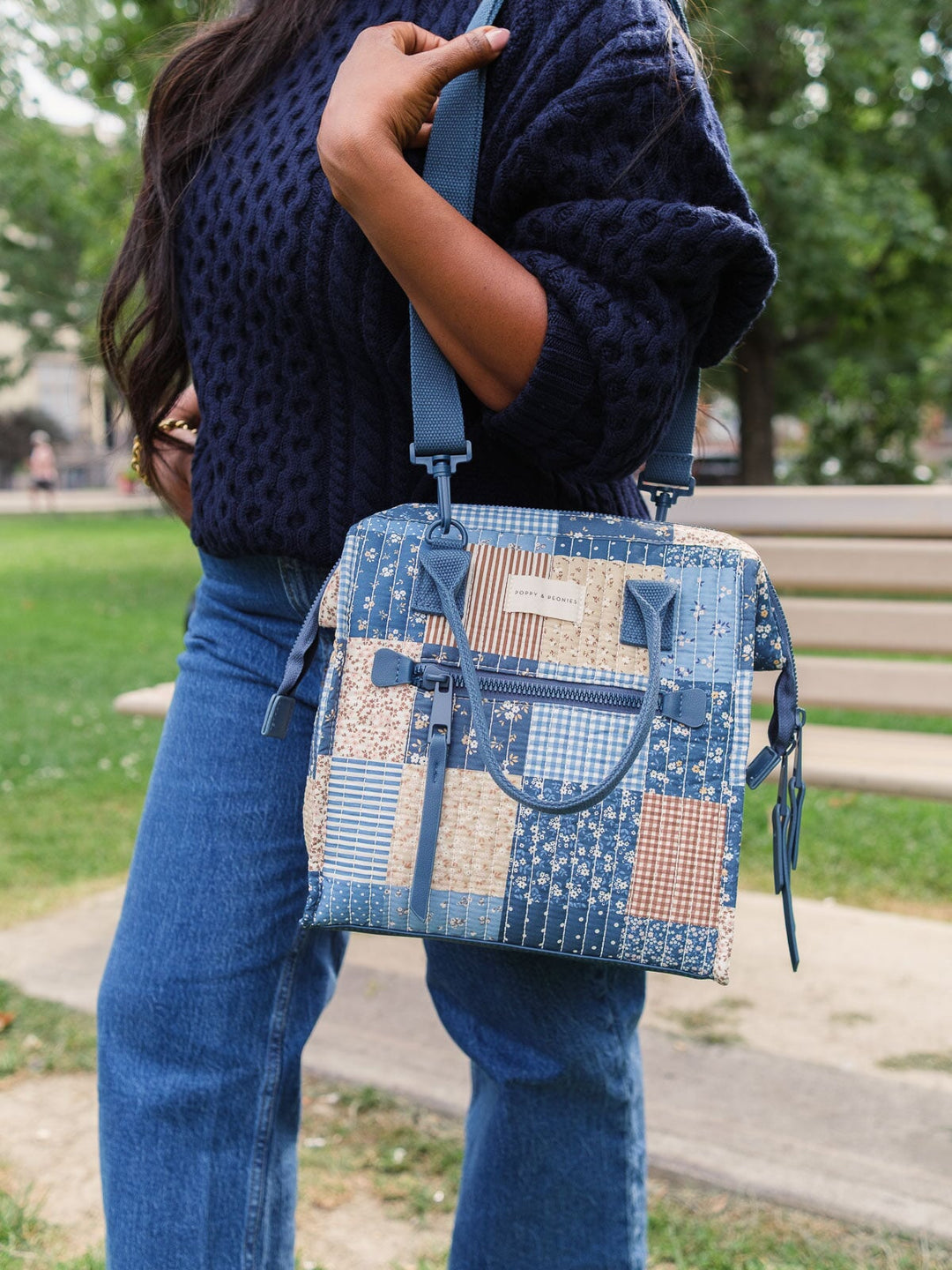 Lifestyle shot of the Poppy & Peonies The Lunch Bag in Navy Patchwork worn over the shoulder, showcasing the adjustable shoulder strap and hands-free carrying op