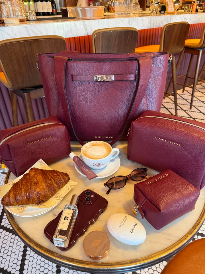 Set of Poppy and Peonies vegan leather products including a handbag, cosmetic cases, and a croissant on a table.