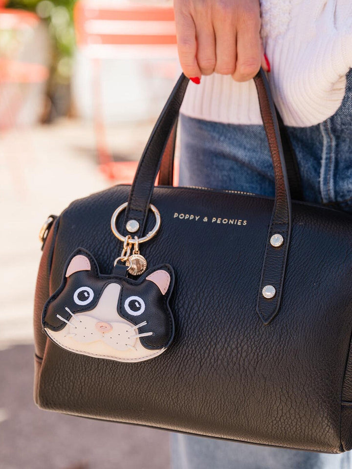 Poppy & Peonies Cat Bag Charm attached to a black handbag, showcasing the playful black and white cat design with gold-tone hardware.