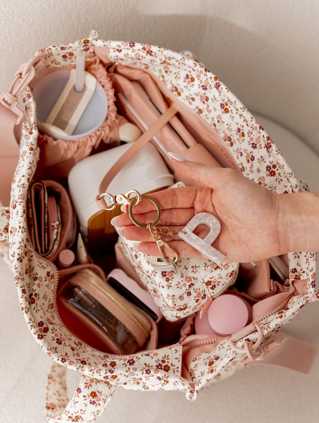 Hand holding a keychain over an open floral-patterned tote bag filled with items.