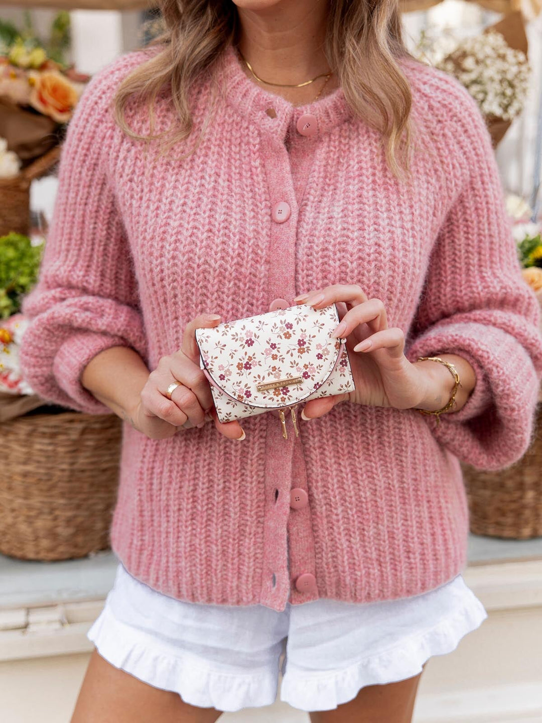 Person wearing a pink knitted cardigan holding a floral wallet.