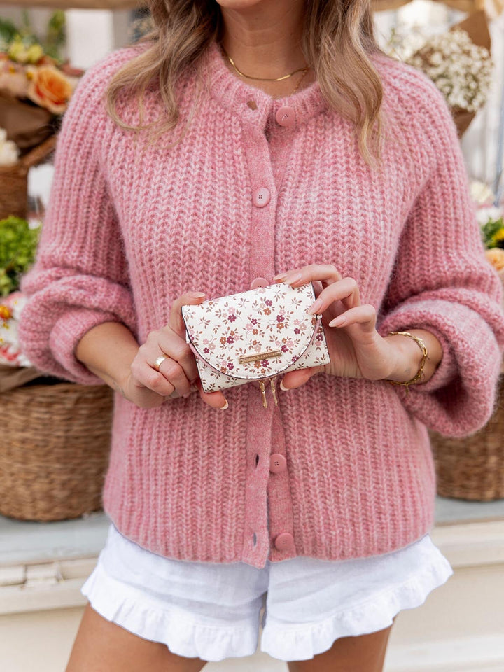 Person wearing a pink knitted cardigan holding a floral wallet.