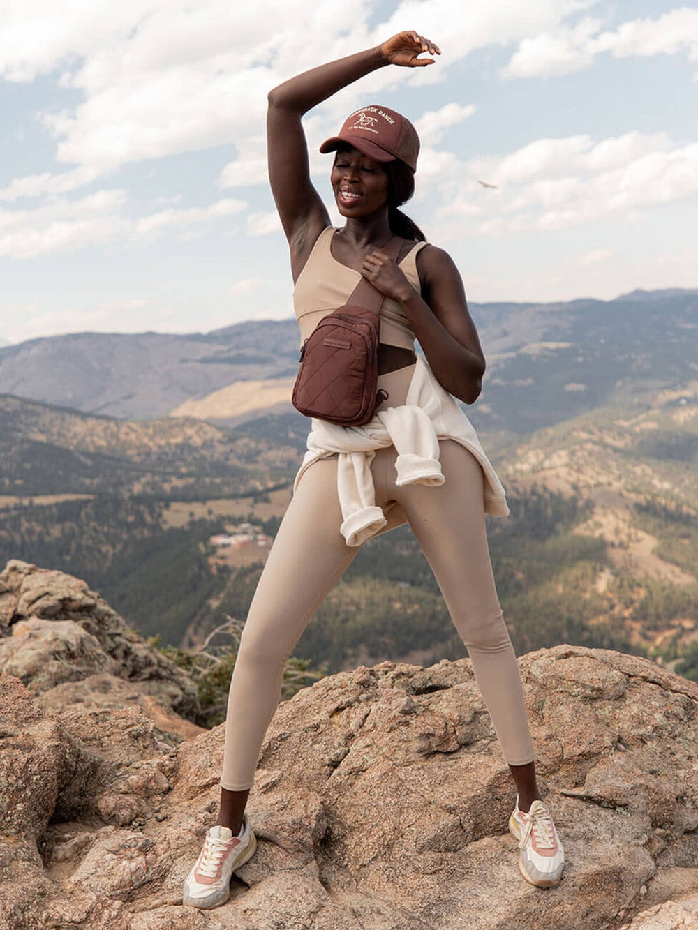 Person wearing a brown quilted sling bag posing on a mountain with a scenic background